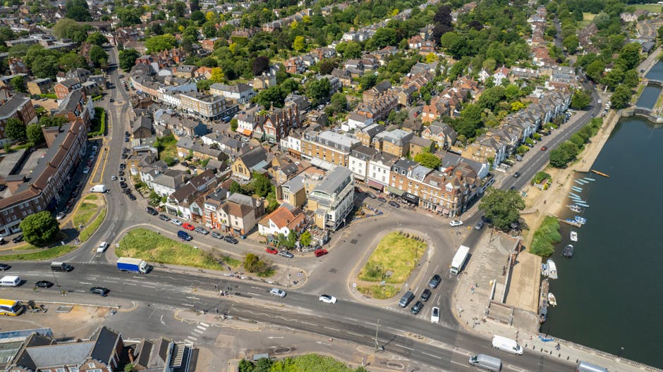 An aerial black-and-white photograph showing a residential neighbourhood with rows of semi-detached and terraced houses along curving streets, parked cars lining the roads and driveways. In the foregr